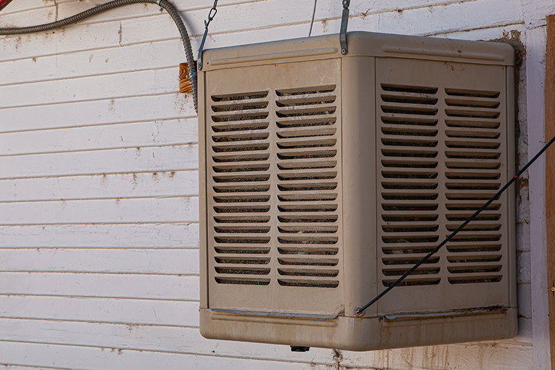 A colored evaporative cooler (commonly known as a swamp cooler) mounted on the exterior wall of a building with white horizontal siding.