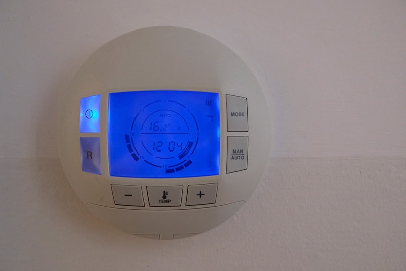 How to Set Your Programmable Thermostat. Photo of a digital thermostat mounted on the wall.