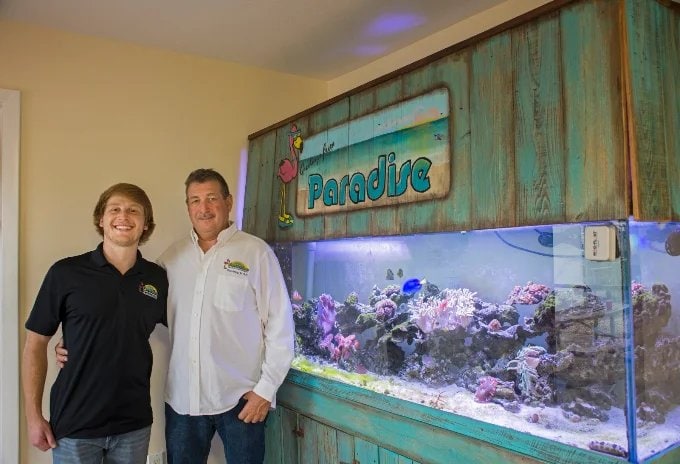 Jason Rich and Matt Rich standing beside the Paradise reef aquarium in the office