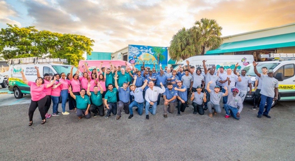 The Paradise team waving in front of the renovated headquarters and service vans at sunset